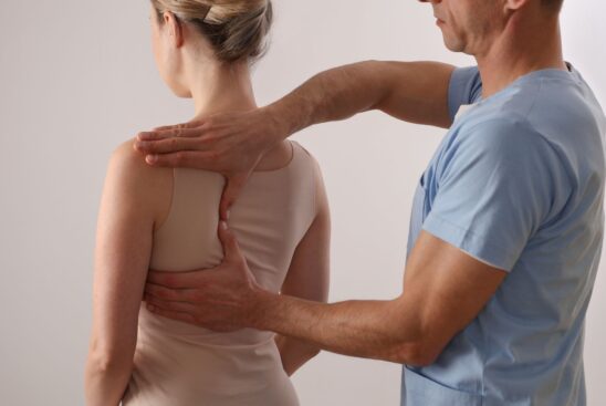 En sjukvårdspersonal i blå uniform undersöker ryggen på en sittande kvinna som bär en beige camisole, eventuellt med tekniker från massage göteborg. En sjukvårdspersonal i blå uniform undersöker ryggen på en sittande kvinna som bär en beige camisole, eventuellt med tekniker från massage göteborg.